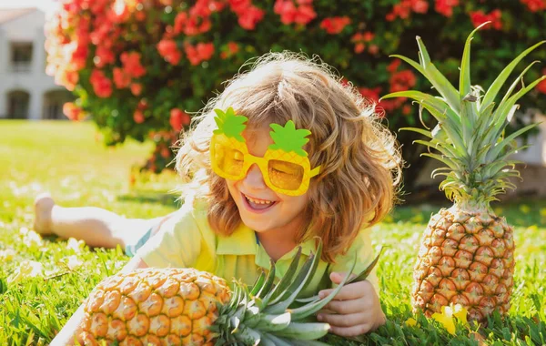 Jovem garoto engraçado segurando abacaxi e sorrindo no quintal. Um miúdo com ananás. Crianças fruta de verão. — Fotografia de Stock