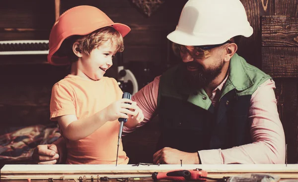 Z 'n zoontje helpt z' n vader met bouwen. Ouder in beschermende helm leren kleine zoon om verschillende gereedschappen te gebruiken in de school workshop. — Stockfoto