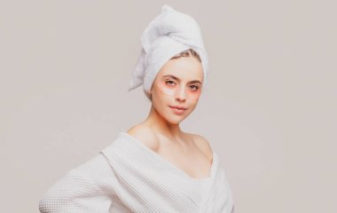 Göz bandı takan bir kadın. Kafasında havluyla portre kızı yakın plan. Göz maskeli kozmetik bantlar. Kadın yakından bakıyor. Gözlerinin altına göz bandı yapıştıran, gözlerinin etrafındaki hassas ciltle ilgilenen bir kadın..