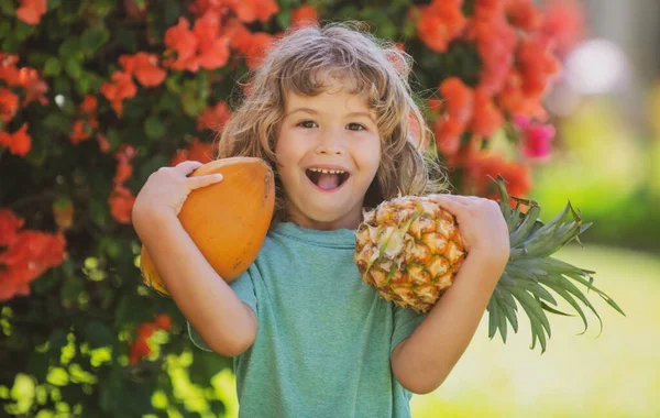 Criança bonito com abacaxi e coco no jardim tropical. Frutas tropicais frescas para crianças. Estilo de vida saudável com frutas tropicais orgânicas frescas. — Fotografia de Stock