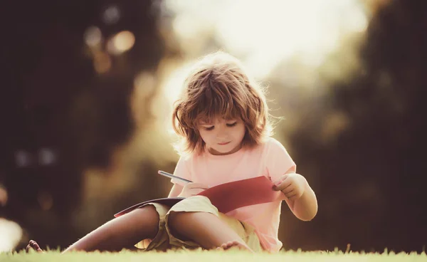 Niños a distancia aprendiendo. Alumno preescolar en el parque en la hierba. —  Fotos de Stock