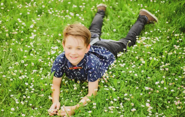 Boldog kisfiú feküdt a fűben a háttérben. Aranyos gyerek élvezi gondtalan életmód mezei virág gyep. — Stock Fotó