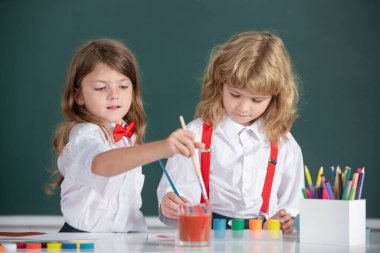 Sınıfta karatahta arka planda komik öğrenciler çiziyor. Okul arkadaşları çocuklar, kız ve erkek birlikte resim yapıyorlar. Erken eğitim.