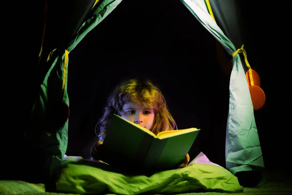 Niños en tienda de campaña niños leyendo libros. Niño leyendo cuento con libro. Los niños se enfrentan con luz nocturna. Concepto de educación y lectura. El desarrollo infantil de la fantasía. —  Fotos de Stock