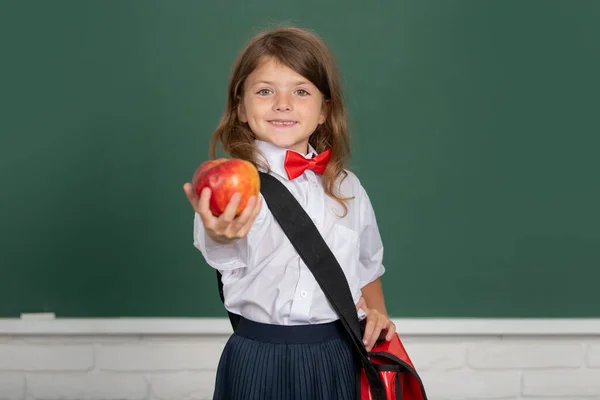 Uma criança gira na escola. Miúdo com maçã vermelha na aula no fundo do quadro negro. Conceito de educação, aprendizagem e crianças. — Fotografia de Stock