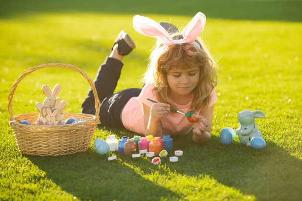 带着复活节彩蛋和兔子耳朵躺在草色彩蛋上的孩子。复活节快乐的孩子们. — 图库照片