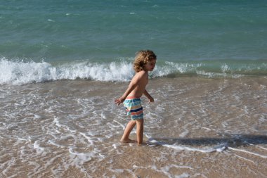 Çocuk deniz dalgalarında zıplıyor. Su birikintilerinden atla. Yaz tatili.