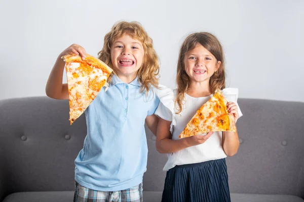 İki çocuk pizza yiyor ve içeride gülümsüyor. Mutlu gülümseyen çocuklar ellerinde pizza dilimleri tutuyorlar.. — Stok fotoğraf