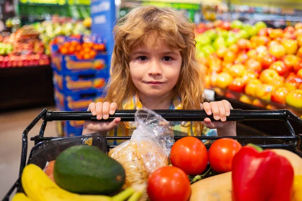 Kind im Supermarkt kauft Obst. Lebensmitteleinkauf für Kinder. Kind mit Wagen, das frisches Gemüse im örtlichen Geschäft auswählt. Kleines Kind wählt frisches Gemüse im Lebensmittelladen. — Stockfoto