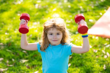 Sağlıklı çocuk hayatı ve spor anlayışı. Çocuk portresi dışarıda halterlerle çalışıyor. Çocuklar için motivasyon ve spor kavramı.