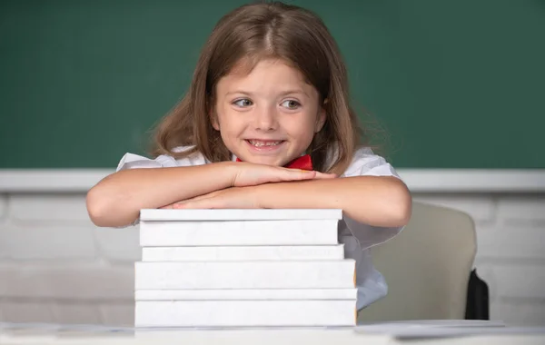 Ragazza sorridente seduta alla scrivania e che tiene per mano i libri in classe. Primo giorno di scuola. — Foto Stock