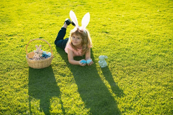Easter kids boy in bunny ears hunting easter eggs outdoor. Cute child in rabbit costume with bunny ears having fun in park. — Zdjęcie stockowe
