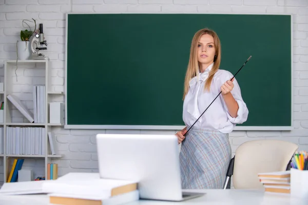 Jonge leraar met wijzer op schoolbord met kopieerruimte. Portret van een jonge, zelfverzekerde en aantrekkelijke studente in de klas. — Stockfoto