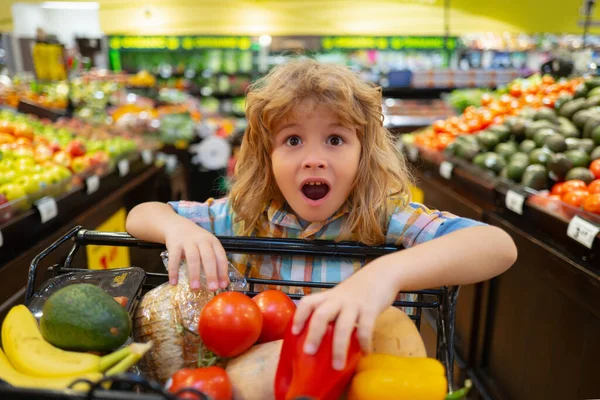 Dziecko w supermarkecie. Zabawny podekscytowany mały chłopiec dowcip zakupy koszyka wybierając towary w sklepie spożywczym lub supermarkecie. Koszyk, koncepcja sklepu spożywczego. — Zdjęcie stockowe