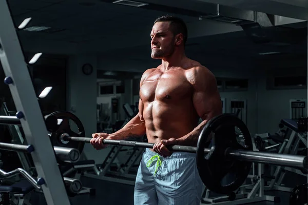 Hombre musculoso haciendo bíceps levantando la barra. Retrato de un joven atleta haciendo ejercicio con mancuerna en el gimnasio. Crossfit, deporte y estilo de vida saludable concepto. — Foto de Stock