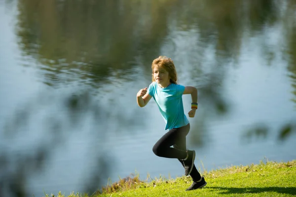 Děti běhají nebo běhají u jezera na trávě v parku. Sportovní běžec běžící v letním parku. Aktivní děti, sportovní děti. Jogging pomáhá tělu být silné. — Stock fotografie
