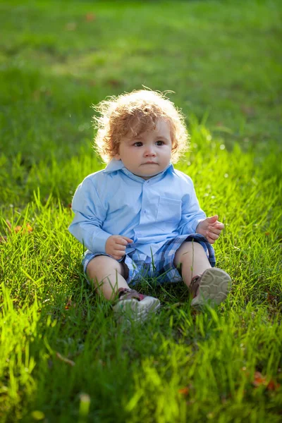 Porträt eines kleinen Jungen, der im Gras sitzt und draußen im Gras spielt. — Stockfoto