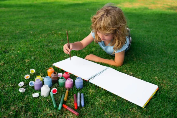 Kinderen maken kunstenaar schildert creativiteit vakantie. Kid trekt in park liggend in gras plezier hebben op de natuur achtergrond. — Stockfoto