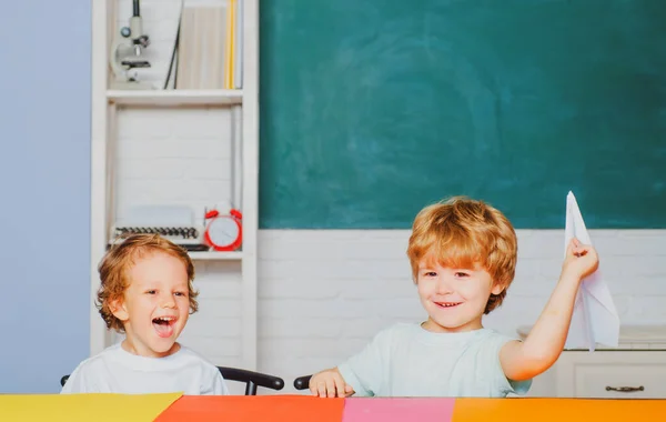 Słodki chłopiec w przedszkolu uczy się w klasie. Proces edukacyjny. Szkoła podstawowa i edukacja. Śmieszne maluchy z podstawówki trzymają papierowy samolot śmiejąc się i uśmiechając. — Zdjęcie stockowe