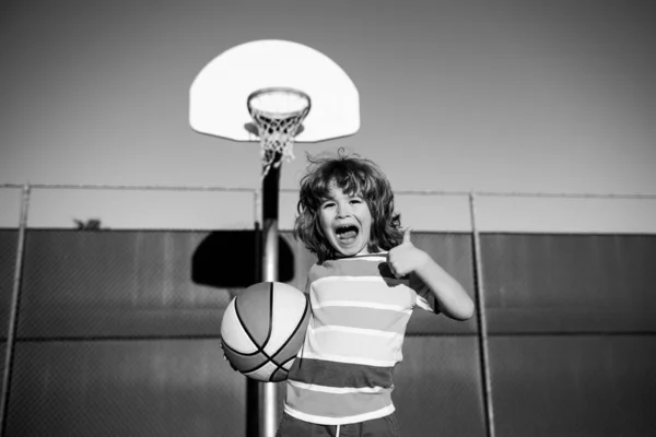 Rapazinho feliz a jogar basquetebol no parque infantil. Retrato de criança desportiva feliz, polegares para cima. — Fotografia de Stock