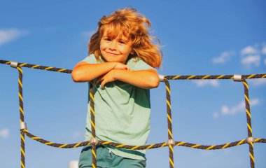 Çocuk yaz günü parkta tepeye tırmanıyor, dışarıda gülümseyerek eğleniyor. Çocuklar oyun oynamaktan, eğlence yaşam tarzından hoşlanıyorlar..