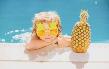 Küçük çocuk tropikal plajda yaz tatilinde açık havuzda mavi suda yüzüyor. Çocuk lüks havuzda yüzmeyi öğreniyor. Yaz ananas meyvesi.