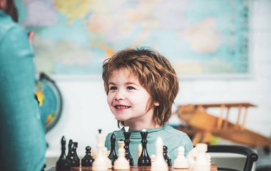 Neşeli gülümseyen küçük çocuk masada oturuyor ve satranç oynarken keyifli bir akşam geçiriyor. Çocuklar erken gelişim.
