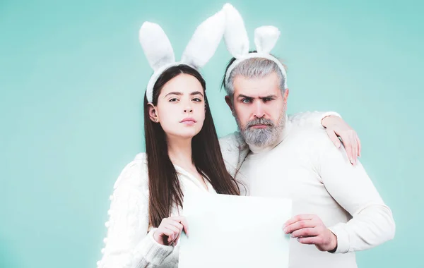 Portrait of Easter couple bunny woman and bunny man hold paper for text. Funny couple dressed in costume Easter bunny on blue background isolated. — Stock Photo, Image