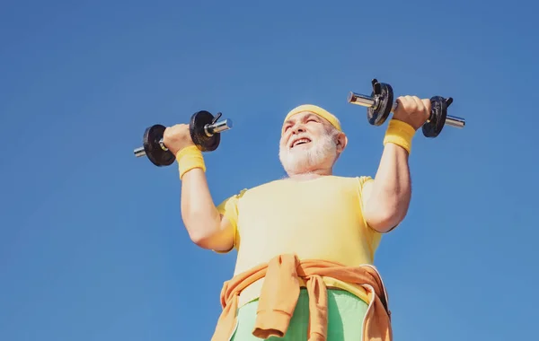 Uomo anziano che solleva manubri. Uomo anziano sulla settantina che si allena e solleva pesi. Un anziano sportivo che solleva manubri. Uomo anziano allenamento. — Foto Stock