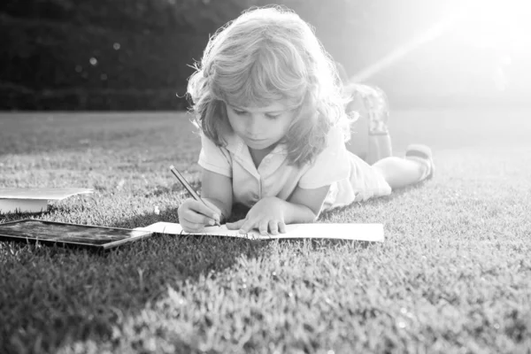 Utomhusporträtt av en söt liten pojke som läser en bok och skriver anteckningar i copybook. Tillbaka till skolan. Barnuppfostran. Förberedelser inför skoldagen och den internationella läskunnighetsdagen. Tillbaka till skolkonceptet. — Stockfoto