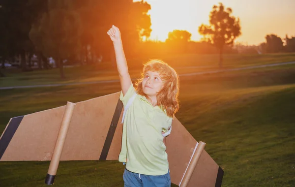 子供たちのリーダーと勝者、成功が始まります。興奮した子供男の子遊びともにおもちゃジェットパック翼スーパーヒーローで公園で日没. — ストック写真