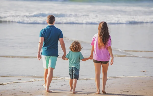 Vista posteriore di felice giovane famiglia che cammina sulla spiaggia. Bambino con genitori che si tengono per mano. Popolo a tutta lunghezza. Viaggi in famiglia, concetto di vacanza. — Foto Stock