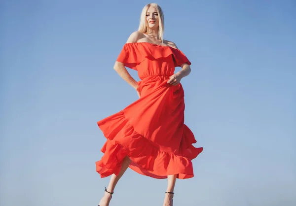 Vrouw in rode jurk beweging aan de hemel. Mooie jonge vrouw in de mode jurk buiten. Sexy en sensueel vrouwelijk model. — Stockfoto
