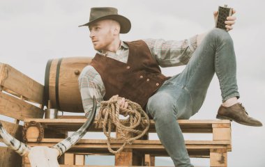 Çiftlikteki kovboy. Kovboy şapkalı ve antika kıyafetli yakışıklı bir adam. Viski içen adam.