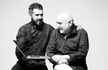 Baba ve oğlunun dizüstü bilgisayarlı portresi. Dizüstü bilgisayarla çalışan iki iş ortağı. Konuşurken ve gülümserken. Oğul babasına modern teknolojiyi kullanmayı öğretiyor..