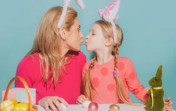 Mother and daughter preparing for Easter and kissing. Cute little child girl with mom wearing bunny ears on Easter day.