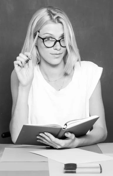 Studentin notiert in der Bibliothek aus einem Buch. Lehrerin sitzt an ihrem Arbeitsplatz und unterrichtet Englisch. Bildungskonzept. Ernsthafte Idee. — Stockfoto