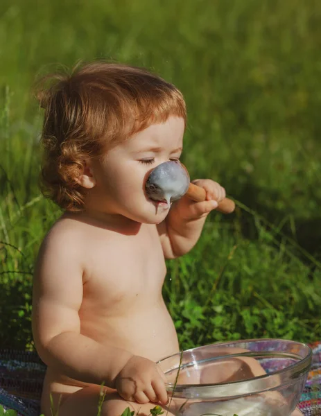 Baby boy eating vegetable mash outdoor on green grass. Carefree childhood in village. — Stock Photo, Image