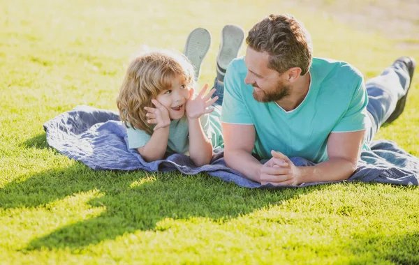 Happy father and son enjoying summer time laying on grass, vacation in a sunny park. — Stock Photo, Image