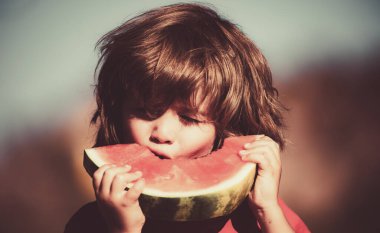 Tatlı karpuz yiyen küçük sevimli çocuğun yakın plan portresi. Karpuz yiyen sevimli bir çocuğun portresi. Çocuk karpuz yiyor..