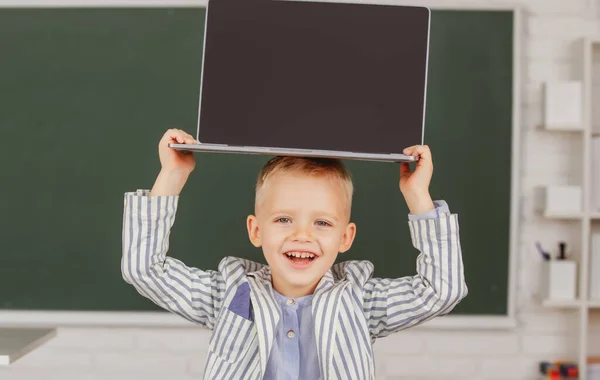 Kleine student jongen met laptop op hoofd in de klas. — Stockfoto