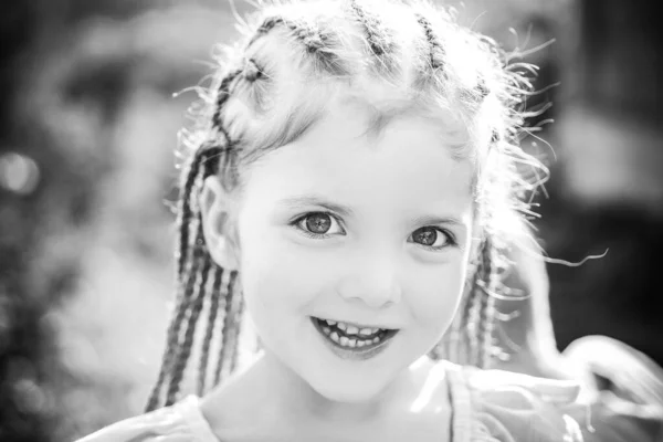 Menina sorrindo criança com dreadlocks penteado. Criança com cabelo na moda no fundo borrão ao ar livre. — Fotografia de Stock