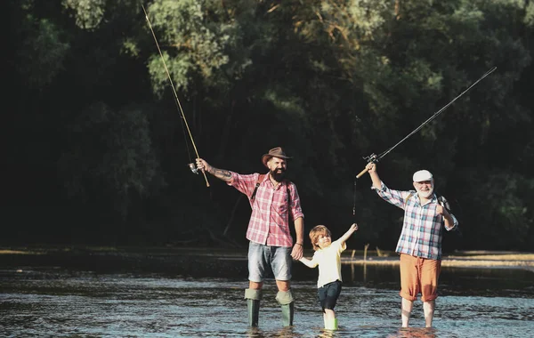 Маленький мальчик на озере с отцом и дедушкой. Отец учит сына ловить рыбу в реке. Счастливого рыбака с удочкой. Летний день . — стоковое фото