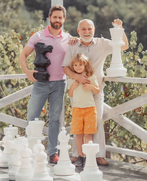 Großvater mit Sohn und Enkel beim Schachspielen. Erstaunte Männer in verschiedenen Altersgruppen beim Schachbrettspiel. Drei Männer. Vatertagskonzept. — Stockfoto