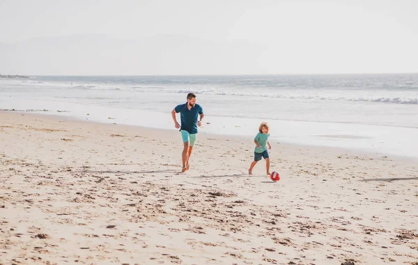 父と息子はビーチでサッカーやサッカーをします。父と子供は屋外で楽しんでいます。家族旅行、休暇、父の日の概念. — ストック写真