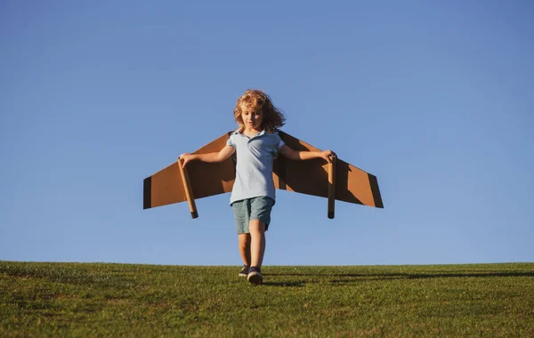 Criança voando em avião feito artesanato de asas de papelão. Sonho, imaginação, infância. Conceito de viagem e férias de verão. Jovem piloto contra um céu azul com cópia cpase. — Fotografia de Stock