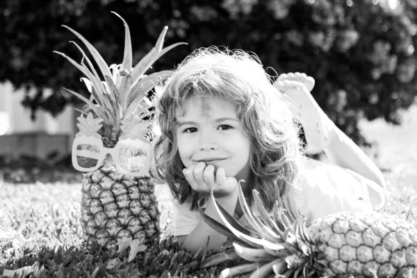 Mladý vtipálek drží ananas a usmívá se na dvorku. Dítě s ananasem. Dětské letní ovoce. — Stock fotografie