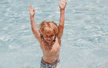 Çocuk yüzme havuzunda yüzüyor ve su sıçratıyor. Eğleniyor, yaz tatili aktiviteleri yapıyor, kollarını açıyor..