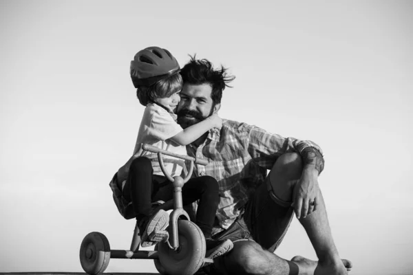 Schöner Vater bringt Sohn Fahrradfahren bei. Glücklicher Papa hilft aufgeregtem Sohn beim Fahrradfahren. Junger lächelnder Junge trägt Helm, während er mit seinem Papa Fahrradfahren lernt. — Stockfoto
