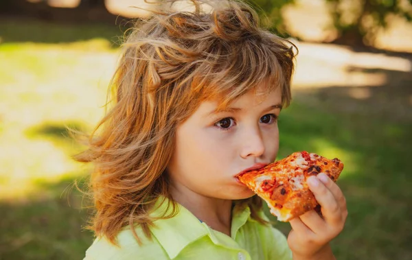 Chłopak je pizzę. Dziecko przyjemność i bierze kawałek pizzy. — Zdjęcie stockowe